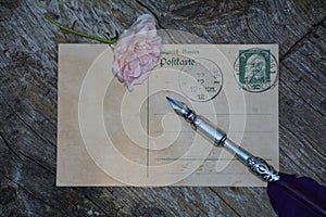 Old blank vintage postcard with old stamp is on old wood with pink rose and nib