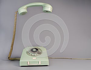 Old blue aged rotary telephone with removed hanging receiver on grey background. Vintage landline home phone with dial