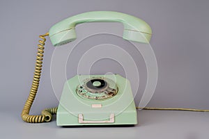 Old blue aged rotary telephone with removed hanging receiver on grey background. Vintage landline home phone with dial