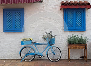 Old blue bicycle stands on the street near the wall with windows with wooden shutters