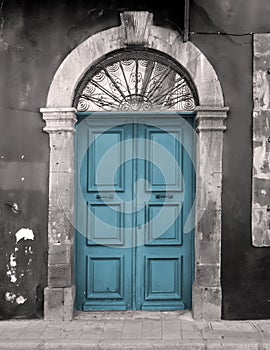 Old blue door in an arched stone frame with flaking back painted walls