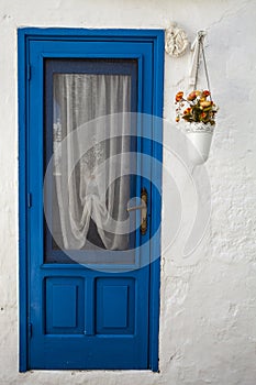 Old blue door of the white house. Flowerpot hanging