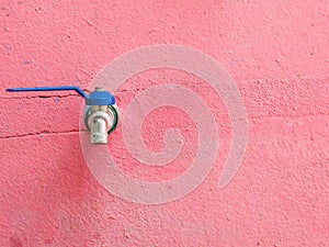 Old blue faucet on the red concrete wall.