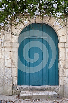 Old blue green door in a stone wall with flowers above