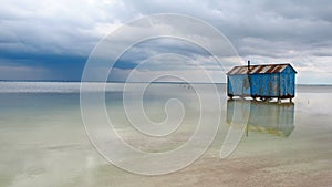 Old blue house abandoned in the middle of the salt lake during an approaching storm. Salar Baskunchak