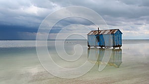 Old blue house abandoned in the middle of the salt lake during an approaching storm. Salar Baskunchak