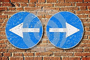 Old blue metallic arrow sign against an aged brick wall indicating to go left and right - concept image