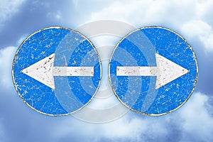 Old blue metallic arrow sign indicating to go left and right against a clody sky - choice, divergence, conflict, contrasts,