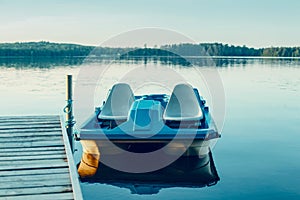 Old blue pedal boat tied to wooden dock pier. Beautiful idyllic calm serene landscape sunset summer view at Canadian Ontario lake