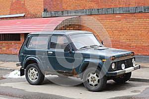 Old blue rusty short-wheelbase Russian jeep parked near a red brick wall