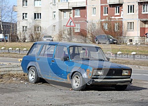 An old blue rusty Soviet car is parked on the street