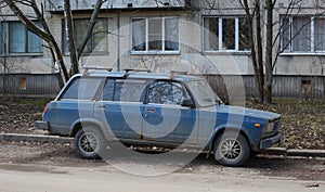 An old blue rusty Soviet car stands near an apartment building