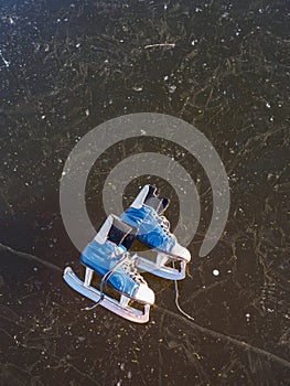 Old blue skates lie on the ice of a frozen lake in the early sunny morning in winter
