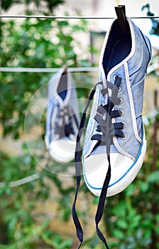 Old blue sneaker hanging on a rope behind a wooden clothespin