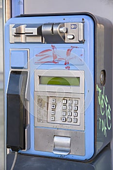 An old blue telephone booth damaged and out of service with signs of deterioration and some banditry painted on it