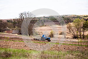 old blue tractor with plow on field and cultivates soil on background of hilly landscape in Ukrainian village. Preparing the soil