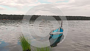 Old blue wooden boat anchored off the coast of the bay sways on calm waves.