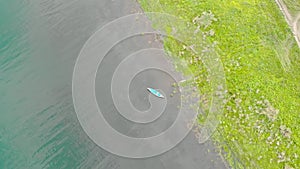 Old blue wooden boat sways on calm waves. Tranquility morning on river. Top view