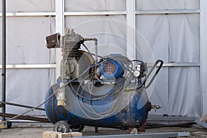 An old blue Working mobile air compressor for painting walls on a construction site. Engineering equipment