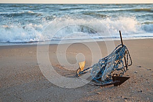 Old boat anchor on the background of the waves of the sea, in the dawn light of the sun