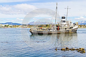 Old boat in Beagle channel with mountains and houses in Ushuaia