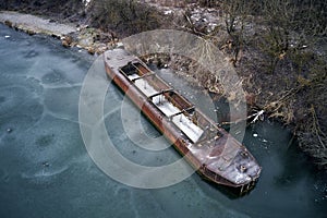 Old boat ship, trapped, frozen in winter ice lake, docked in pier, aerial top down view
