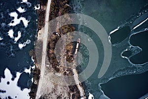 Old boat ship, trapped, frozen in winter ice lake, docked in pier, aerial top down view