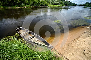 Old boat tied with chain and padlock at green summer bank at noon on Neman river in Grodno Belarus shot wide