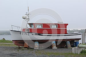 An old boat or yacht propped up on rusting barrels and for sale on a foggy day in Mulgrave on the Strait of Canso. photo