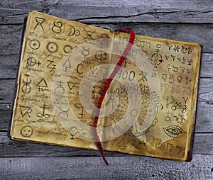 Old book with alchemic symbols lying on the wooden table