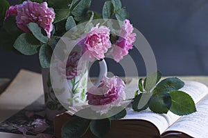 An old book with a bouquet of ancient pink roses in a vintage cup, summer reading concept