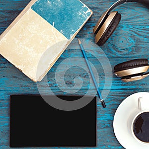 Old book, cup of coffee, tablet, pencil and headphones on dark wooden background