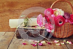 Old book and glasses next to flowers on wooden table