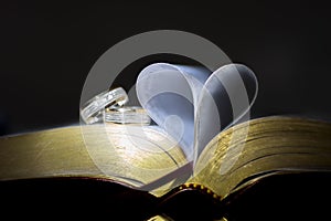 Old book with heart-shaped pages. Ring between pages, black background. photo