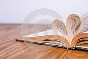Old book and heart-shaped pages. White background. Wooden Table