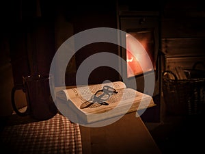 An old book, a mug and glasses in front of an woodstove