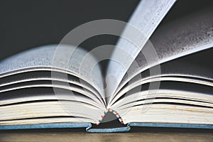 An old book open on wooden table with black color wall background copy space