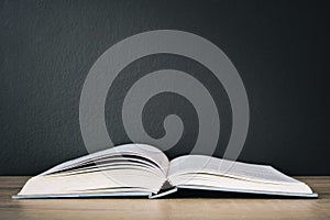 An old book open on wooden table with black color wall background and light from above, copy space