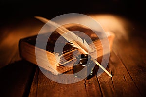 Old book with quill pen and inkwell on wooden table