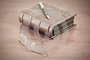 Old book with reading glasses and pen