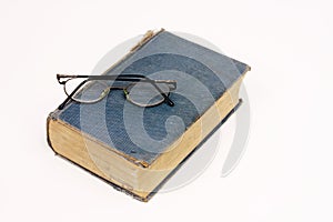 Old book with reading glasses resting on white