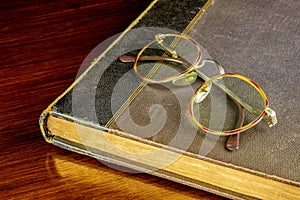 Old Book and Spectacles on a Polished Wooden Table Top