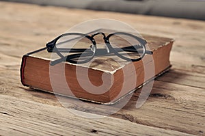 Old book with vintage glasses on a wooden table