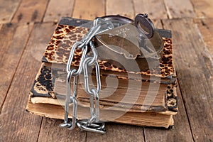 Old books bound by a new shiny chain with an old padlock. Forbidden old works artists on a wooden table