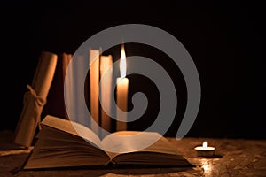 Old books, a burning candle and a scroll on a wooden table on a