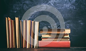 Old books and eye glasses on blackboard background