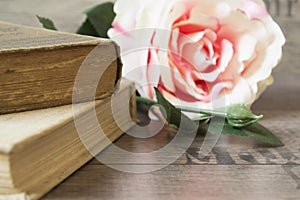Old books and flower rose on a wooden background. Romantic floral frame background. Picture of a flowers lying on an antique book