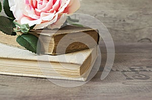 Old books and flower rose on a wooden background. Romantic floral frame background. Picture of a flowers lying on an antique book