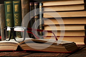 Old books and reading glasses on desk in library room