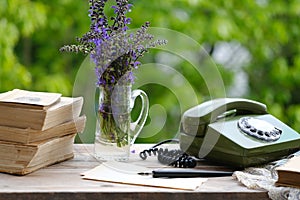 old books, rotary telephone, wild flowers on old wooden table in garden, remote work in summer in retro style, beautiful blurred